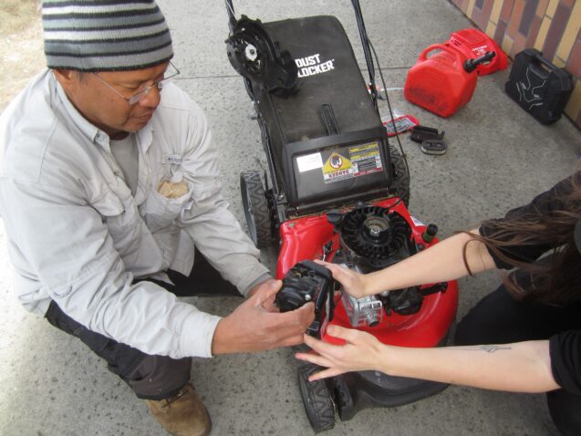Fixit coach assisting a resident with fixing his red lawn mower and showing him the battery system.